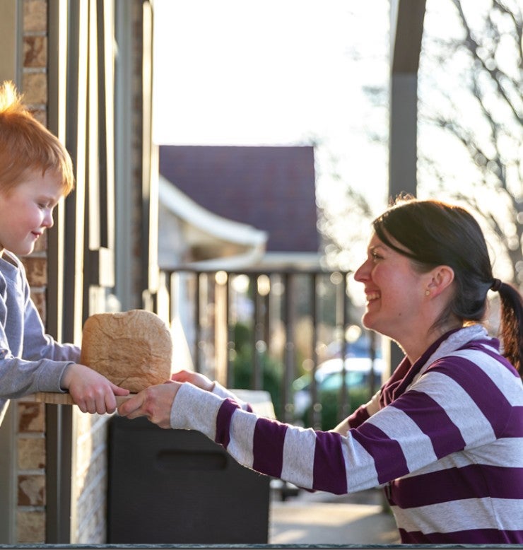 Woman handing a small boy a fresh loaf of bread.